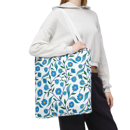 Person wearing a light hoodie and dark pants holds the Blue Floral Tote Bag, featuring a vibrant pattern of blue flowers and green leaves, ideal for joyful summer outings.