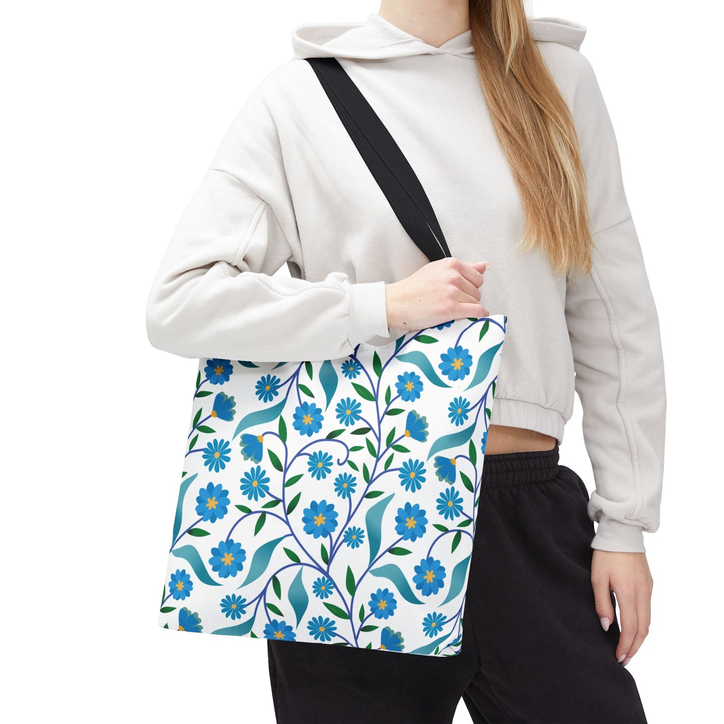 Blue Floral Tote Bag with a pattern of blue flowers, green leaves, and vines, carried by a person in a hoodie. Ideal for summer outings, offering durability and cheerful style.