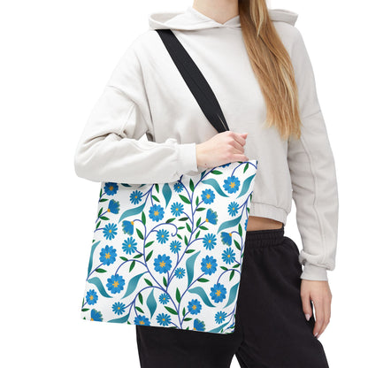 Blue Floral Tote Bag with a pattern of blue flowers, green leaves, and vines, carried by a person in a hoodie. Ideal for summer outings, offering durability and cheerful style.