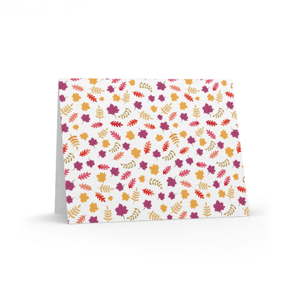 Autumn Greeting Cards — Pack of 8/16/24 featuring a vibrant edge-to-edge autumn-leaf pattern in reds, golds, and purples on a white background, folded with a matching white envelope for personalized messages.