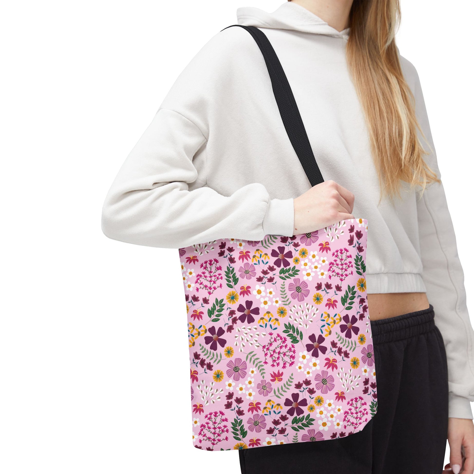 The Floral Tote Bag showcases a vibrant pink floral pattern with purple, yellow, and white blossoms, featuring black straps. Ideal for everyday use, it complements the casual, stylish look of FireBrook Essentials.