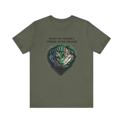 Crocodile: Walk in Silence, Strike with Purpose Bella+Canvas Unisex T-Shirt featuring a detailed graphic of a green alligator with yellow eyes, capturing a sense of stealth and determination.