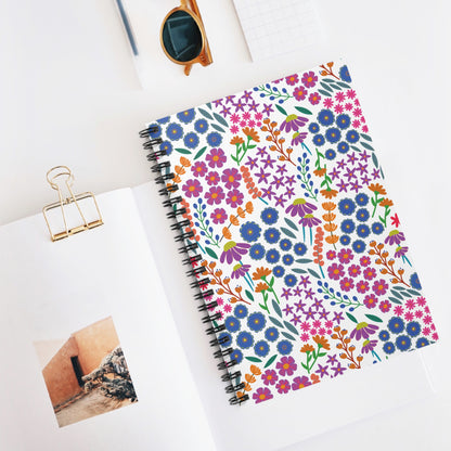 Floral Spiral Notebook with a vibrant cover, surrounded by tortoiseshell sunglasses, graph paper, and a book featuring adobe architecture, embodies FireBrook Essentials' blend of creativity and joy in everyday items.