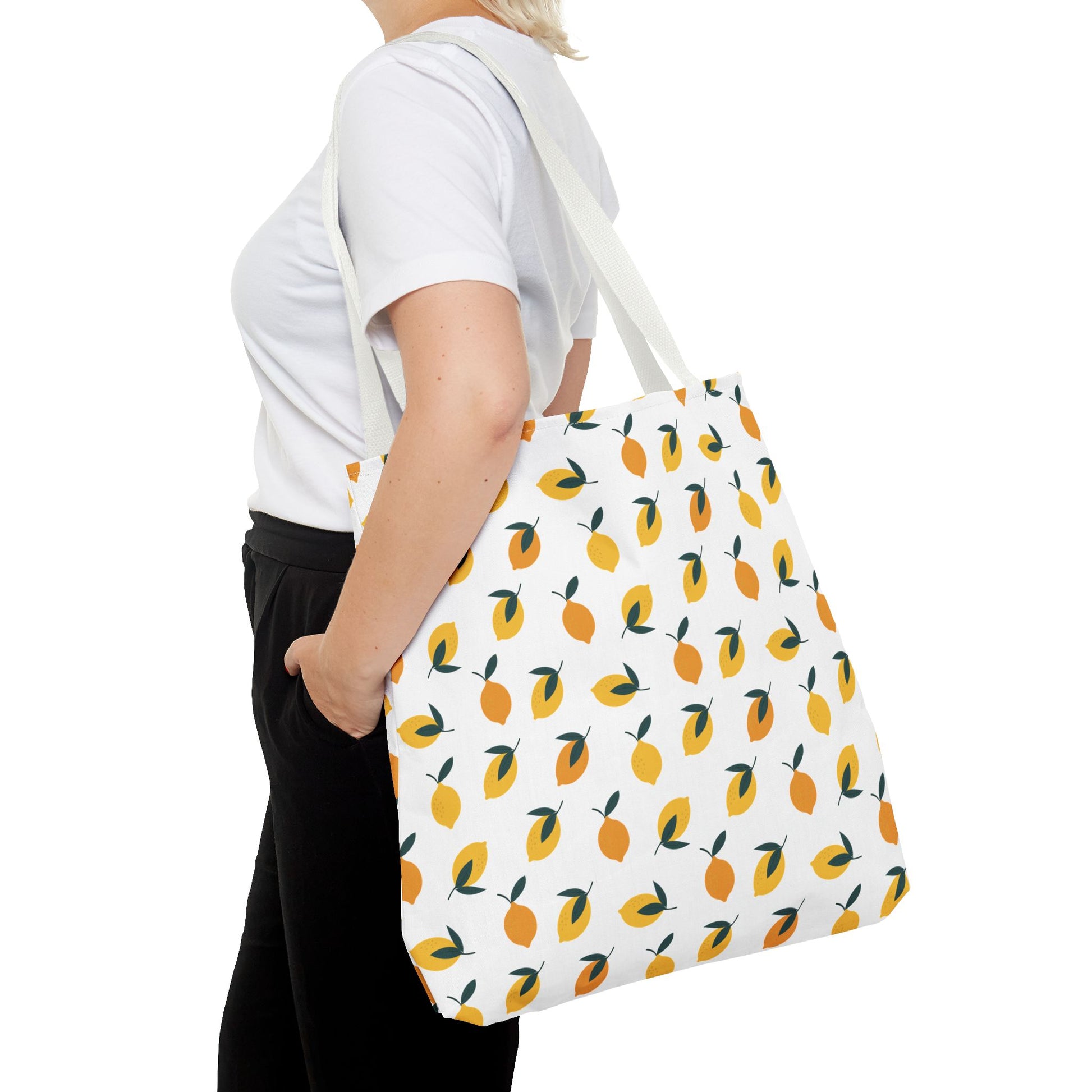 Lemon Drop Toss Tote Bag over shoulder, featuring a vibrant, stylized lemon pattern, ideal for summer outings. Perfectly complements black pants and white T-shirt. Durable, cheerful design by FireBrook Essentials.