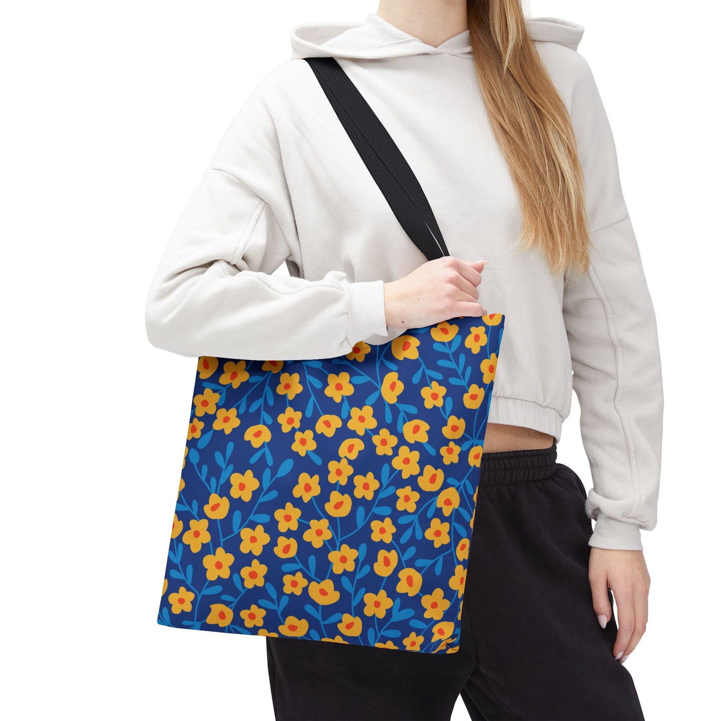 Floral Tote Bag with yellow-orange flowers and blue leaves on deep blue, carried over the shoulder by a person in a light hoodie. Ideal for stylish, joyful outings.