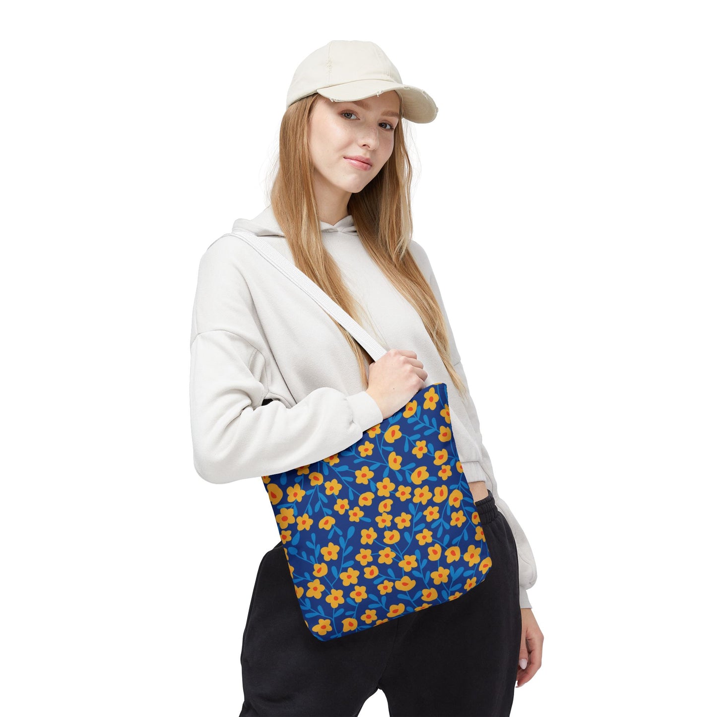 Young woman wearing light-colored attire carries the Cobalt Poppy Field Tote Bag, showcasing its bright floral design with yellow-orange flowers and blue leaves, embodying FireBrook Essentials’ uplifting and stylish aesthetic.