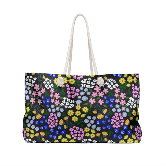The Weekender Bag, featuring a dense multicolored floral pattern with a rope-style handle, embodies stylish practicality, ideal for weekend trips. Its generous size and vibrant design suit joyful, effortless travel.