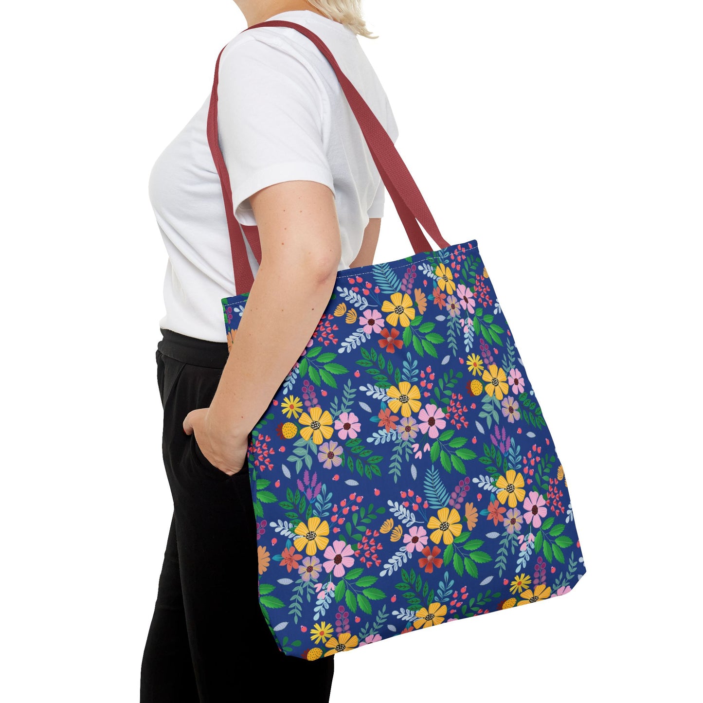 Person carrying the Deep Sea Floral Patch Tote Bag with burgundy straps, displaying vibrant yellow, pink, and orange flowers against a deep blue backdrop. Ideal for summer adventures or market trips.