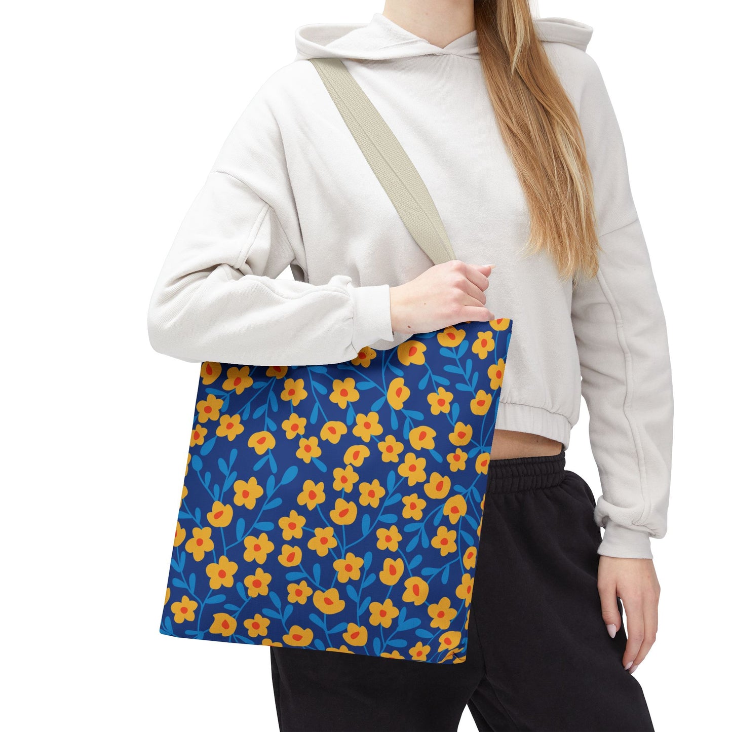 A person wears a light cropped hoodie and dark pants, carrying the Cobalt Poppy Field Tote Bag—a deep blue floral tote with yellow-orange blossoms, perfect for joyful summer outings.