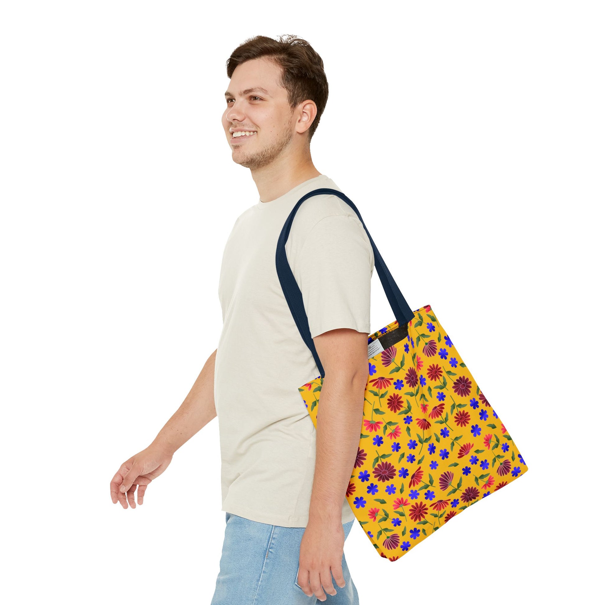 Young man walking with a Golden Wildflower Tote Bag, featuring vibrant red, blue, and pink flowers on a yellow background with black straps, embodying cheerful, practical style from FireBrook Designs.