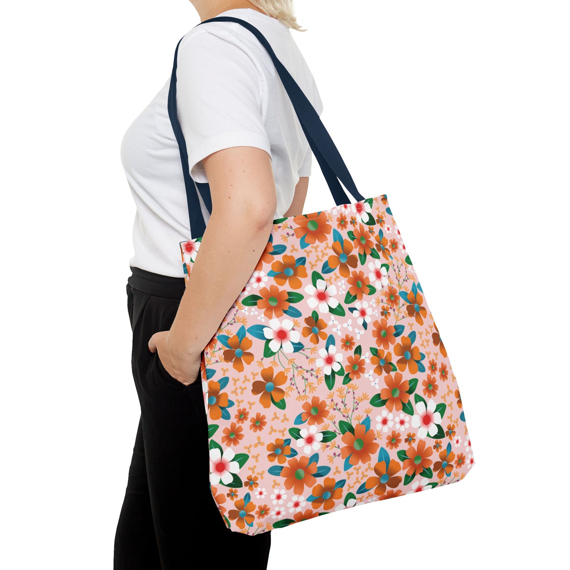 Peach Poppy Grove Tote Bag features a vibrant floral pattern with orange, white, teal, and green blossoms on light pink, complemented by dark navy straps, embodying FireBrook Designs' joyful and stylish essence.