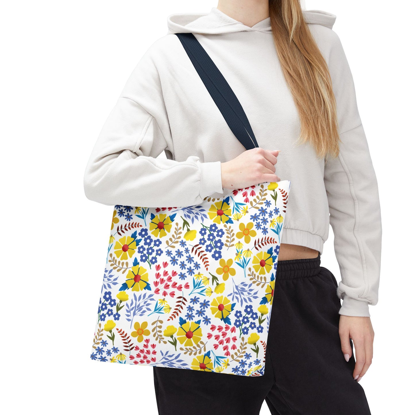 Floral Tote Bag with vibrant red, yellow, and blue flowers, carried by a person in a beige hoodie, featuring a durable polyester body and navy-blue strap, ideal for lively summer outings.