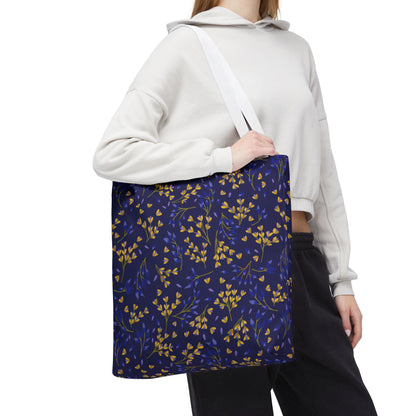 Person wearing a light-colored hoodie and dark pants carries the Floral Tote Bag, featuring a navy-blue background with yellow and blue botanical motifs, ideal for stylish summer outings.