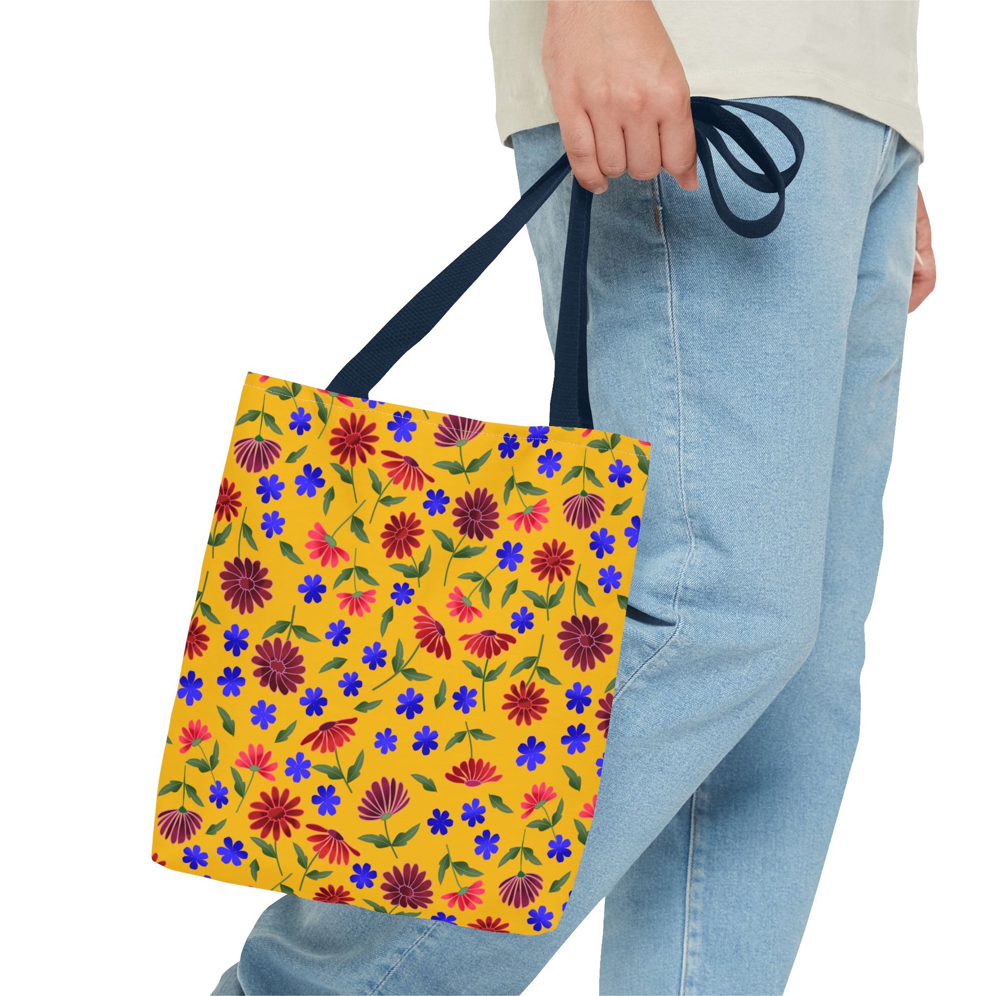 Golden Wildflower Tote Bag with vibrant floral patterns and dark navy straps, held by a person in light-wash jeans and a neutral top. A cheerful, practical accessory for everyday use.