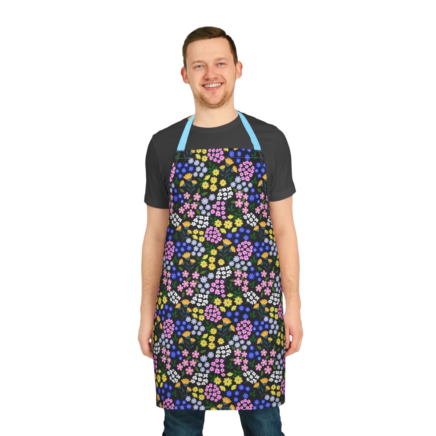 Smiling man models the Apron Floral Design from FireBrook Essentials, featuring a colorful floral pattern on black, with light-blue straps. Ideal for adding joy and comfort to cooking and crafting activities.
