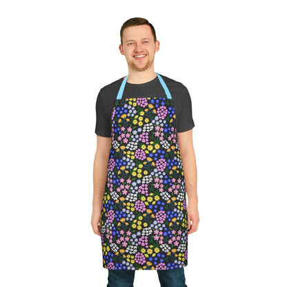 Smiling man models the Apron Floral Design from FireBrook Essentials, featuring a colorful floral pattern on black, with light-blue straps. Ideal for adding joy and comfort to cooking and crafting activities.