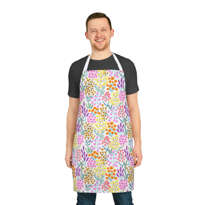 Floral Apron: A smiling young man wears a vibrant, multicolored floral-patterned apron over a black T-shirt, highlighting FireBrook Designs' blend of comfort and style with its stain-free, 100% polyester fabric.