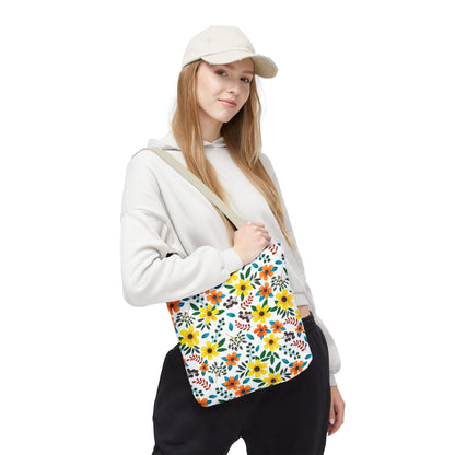 The Sunny Meadow Mix Tote Bag, featuring vibrant yellow, orange, and teal flowers with green leaves, is slung over a woman's shoulder, complementing her casual white hoodie and dark pants.
