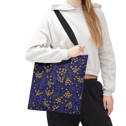 Floral Tote Bag: A deep navy canvas tote with yellow and blue floral patterns, featuring sturdy black straps, showcased by a person in a light hoodie, perfect for cheerful, stylish summer outings.
