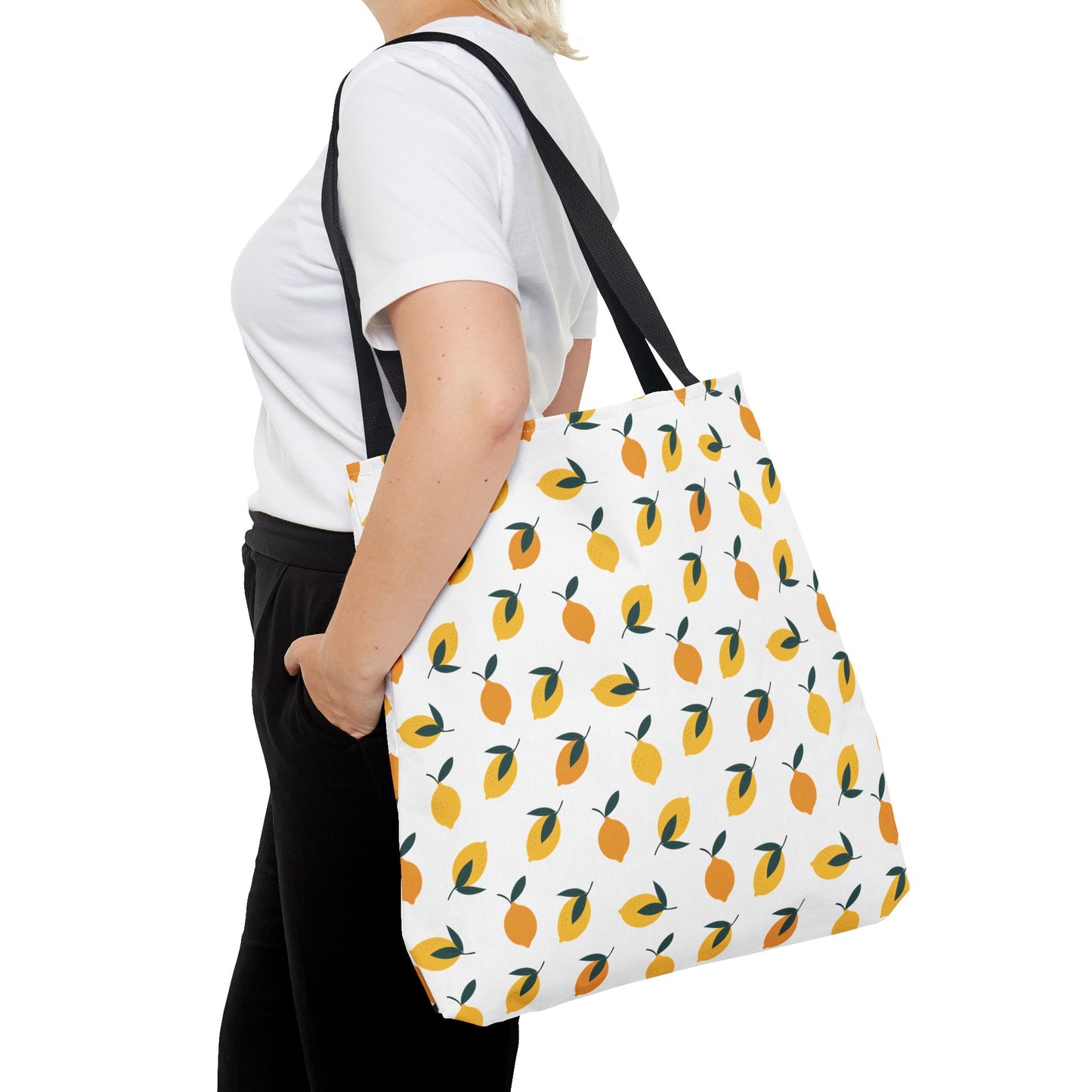 Lemon Drop Toss Tote Bag showcased on a person, featuring a lively lemon pattern with green leaves on white canvas, black straps, embodying FireBrook Essentials' commitment to joyful, stylish functionality.