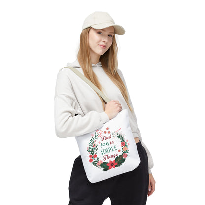Woman wearing a hat and sweatshirt holding the Find Joy in Simple Things tote bag with a floral design, showcasing its stylish and functional appeal.