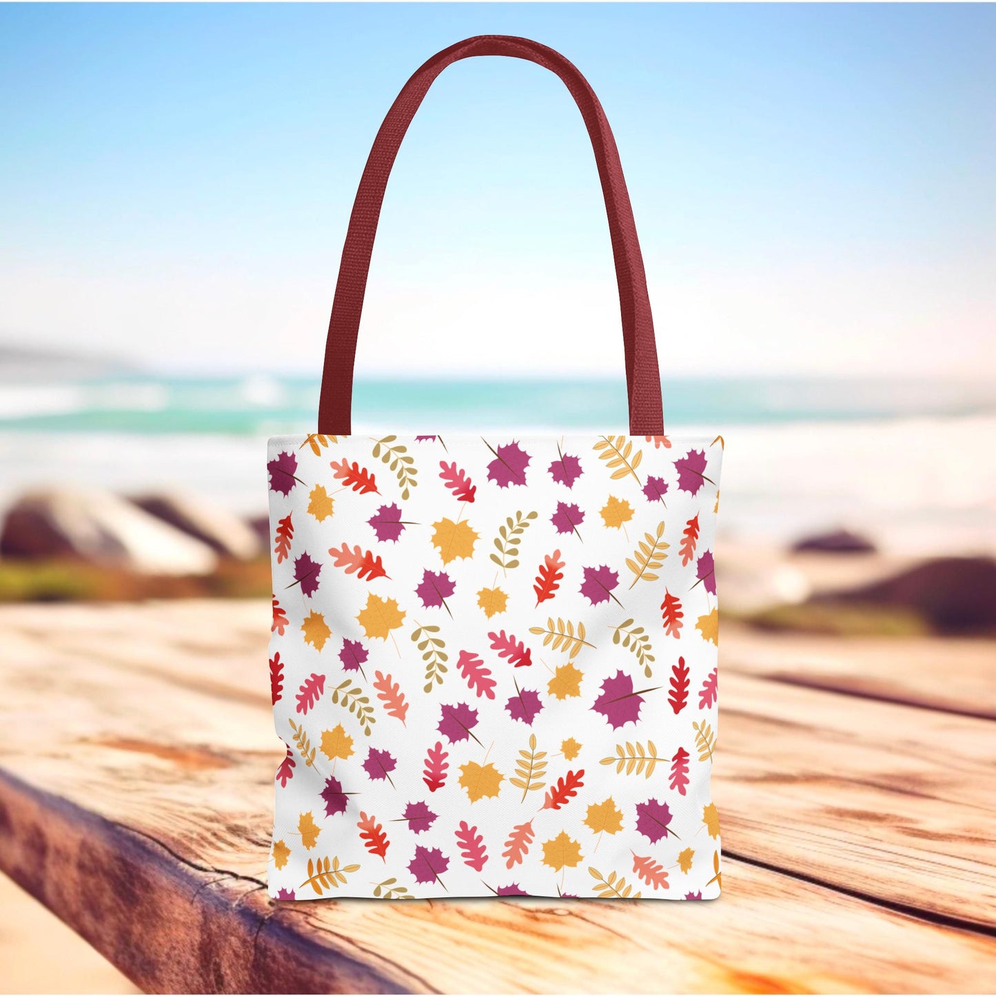 The Autumn Leaves Tote Bag features a white canvas with a vibrant fall foliage pattern, complete with burgundy-red straps, capturing FireBrook Essentials' blend of style and practicality for everyday use.