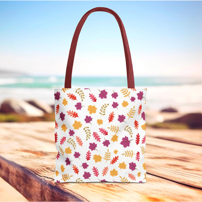 The Autumn Leaves Tote Bag features a white canvas with a vibrant fall foliage pattern, complete with burgundy-red straps, capturing FireBrook Essentials' blend of style and practicality for everyday use.