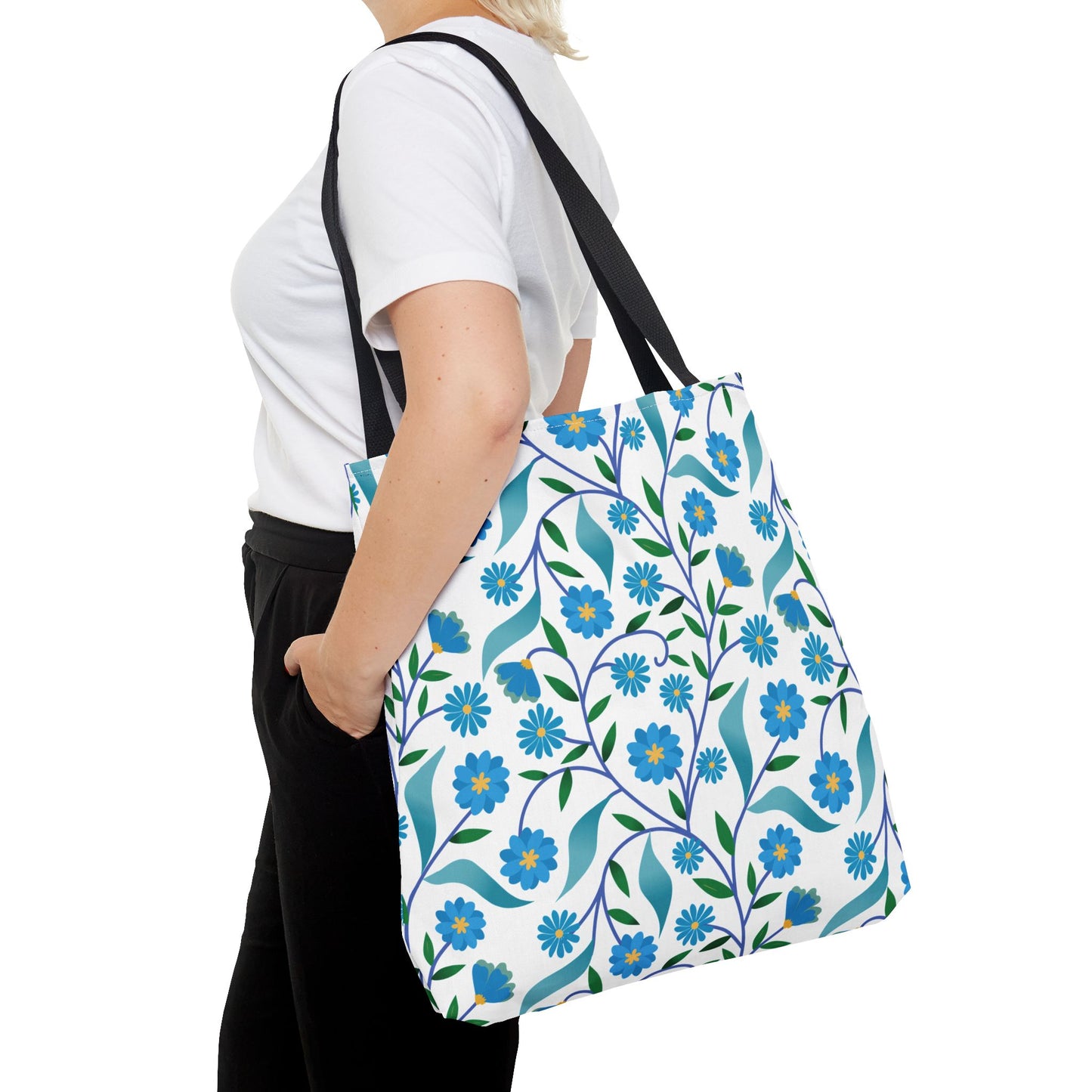 Side view of a person carrying the Blue Floral Tote Bag, featuring vibrant blue flowers and green leaves on a white background. The bag has black straps, ideal for summer outings and joyful experiences.