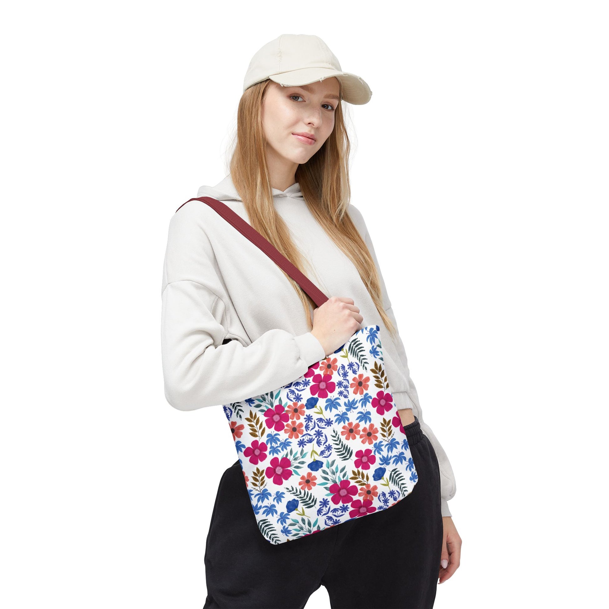 Young person wearing a light-beige baseball cap and pale hoodie, holding the Confetti Wildflower Tote Bag, featuring a vibrant floral pattern and burgundy strap, perfect for adding cheer to any outing.
