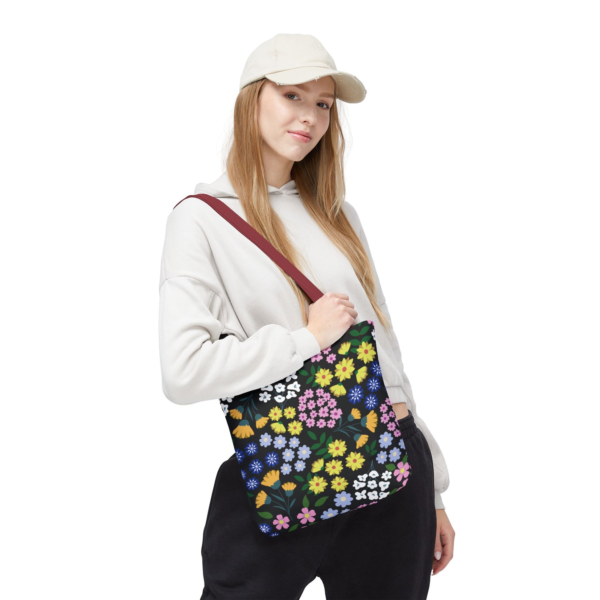 Floral Tote Bag with vibrant blossoms and green leaves on a black background, carried by a casually dressed person. Features a dark red strap, ideal for stylish summer outings.