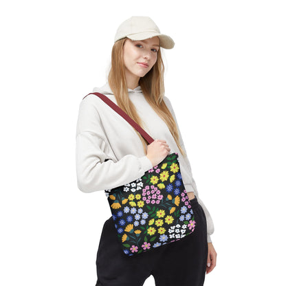 Floral Tote Bag with vibrant blossoms and green leaves on a black background, carried by a casually dressed person. Features a dark red strap, ideal for stylish summer outings.