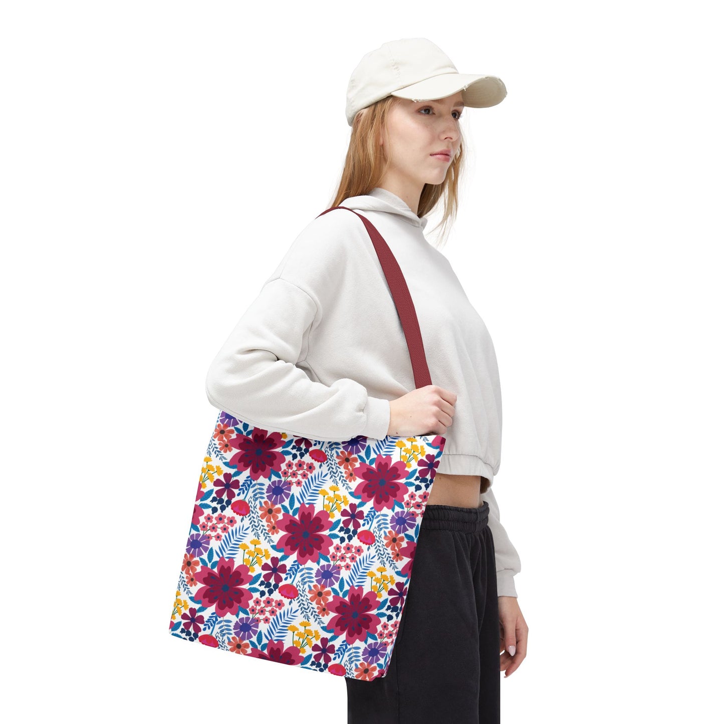 A woman carries the Violet Daisy Carnival Tote Bag featuring vibrant floral patterns, complemented by a burgundy strap, embodying FireBrook Designs' ethos of style and joy.
