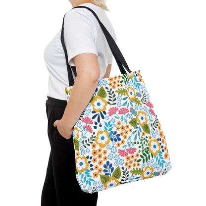 Person wearing a plain white T-shirt and black pants, carrying the Floral Tote Bag with black straps. The bag features a vibrant floral print, ideal for summer outings and showcasing FireBrook Designs' uplifting style.