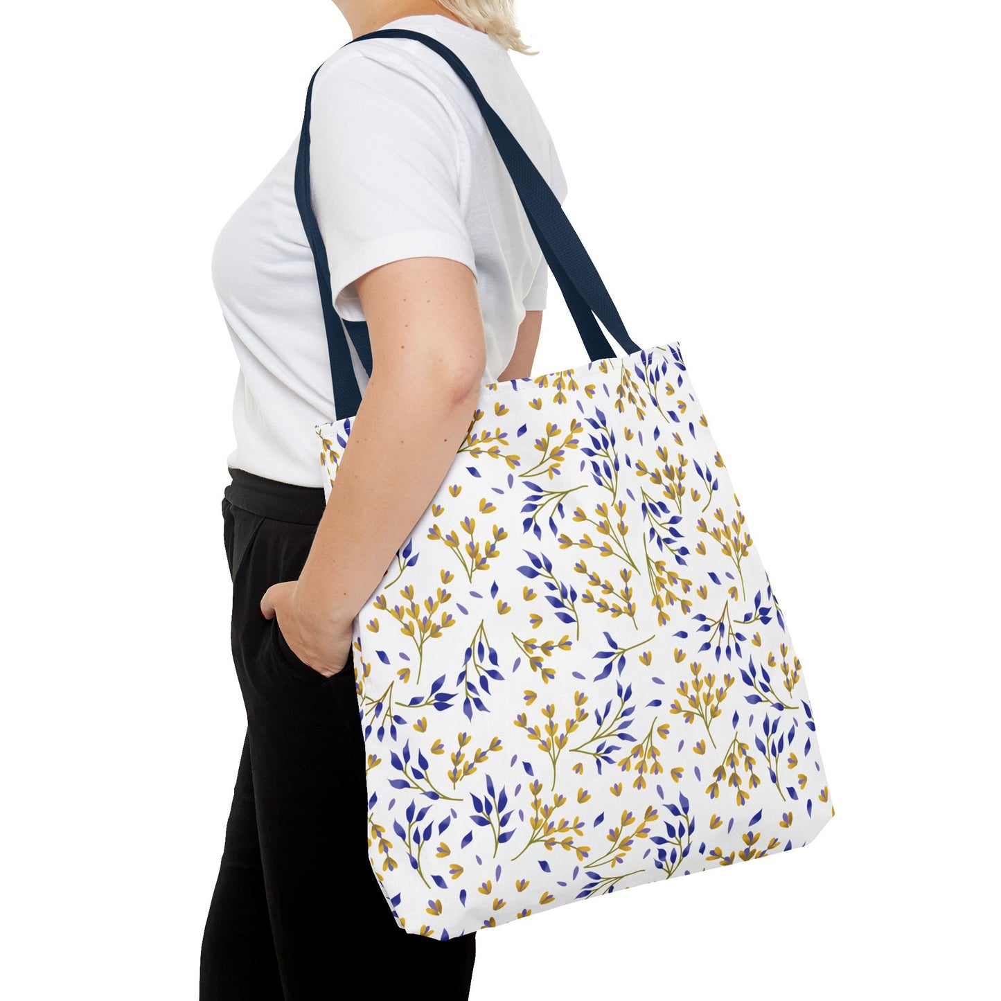 The Floral Tote Bag, featuring a delicate botanical pattern of yellow and blue leaves, complements a casual outfit. Its navy blue straps add contrast, perfect for stylish, cheerful summer outings.