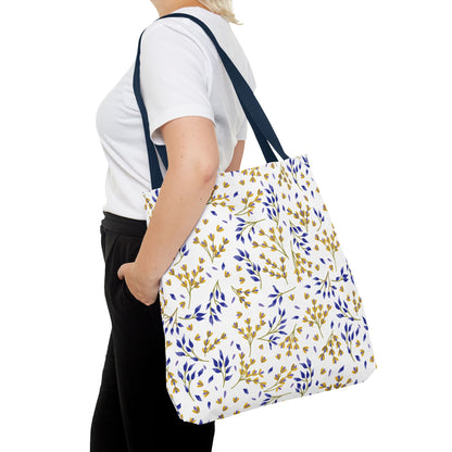 The Floral Tote Bag, featuring a delicate botanical pattern of yellow and blue leaves, complements a casual outfit. Its navy blue straps add contrast, perfect for stylish, cheerful summer outings.