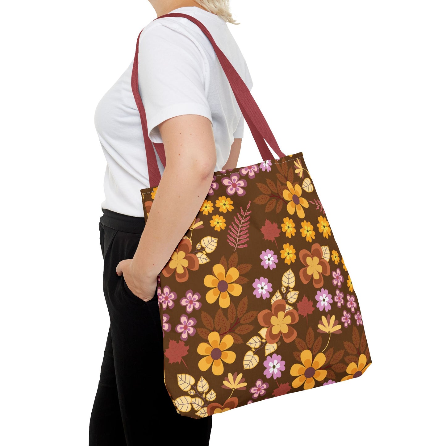 Floral Tote Bag featuring vibrant flowers and leaves in yellow, orange, rust, and pale purple on a dark brown canvas, draped over a shoulder with burgundy-red straps, embodies FireBrook Essentials' cheerful, uplifting designs.