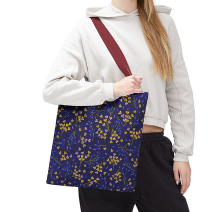 Person wearing a light-colored hoodie and dark pants carrying the Floral Tote Bag, featuring a navy-blue background with yellow and blue leaves, and a wide reddish-brown strap, embodying FireBrook Designs' uplifting style.