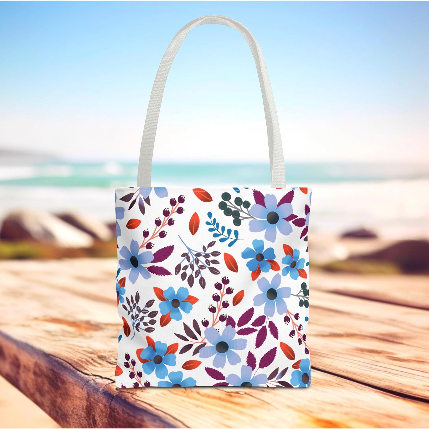 Floral Tote Bag featuring a vibrant blue and purple floral pattern with red-orange leaves, ideal for summer outings. Durable polyester construction with reinforced handles, embodying FireBrook Designs' uplifting style and practicality.