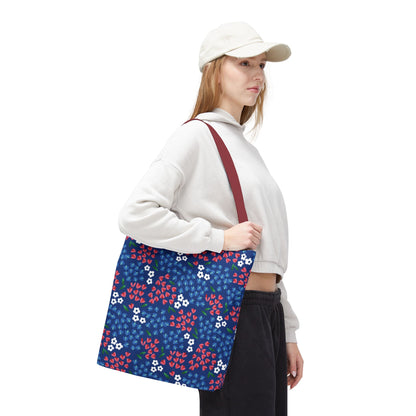 Model carrying a Floral Tote Bag featuring red and white flowers on navy-blue. The bag, with a contrasting red strap, complements her casual outfit, embodying FireBrook Essentials' cheerful and stylish design ethos.