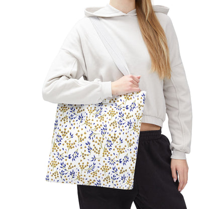 Person wearing a light-gray hoodie holds the Wild Herb Garden Tote Bag, featuring a soothing pattern of leafy branches in muted gold and deep blue, perfect for joyful summer or market adventures.