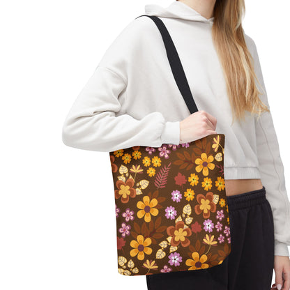 A person carries the Floral Tote Bag, featuring vibrant yellow, orange, rust-red, and pale pink flowers on a dark brown background, complemented by a solid black strap, perfect for joyful summer outings.