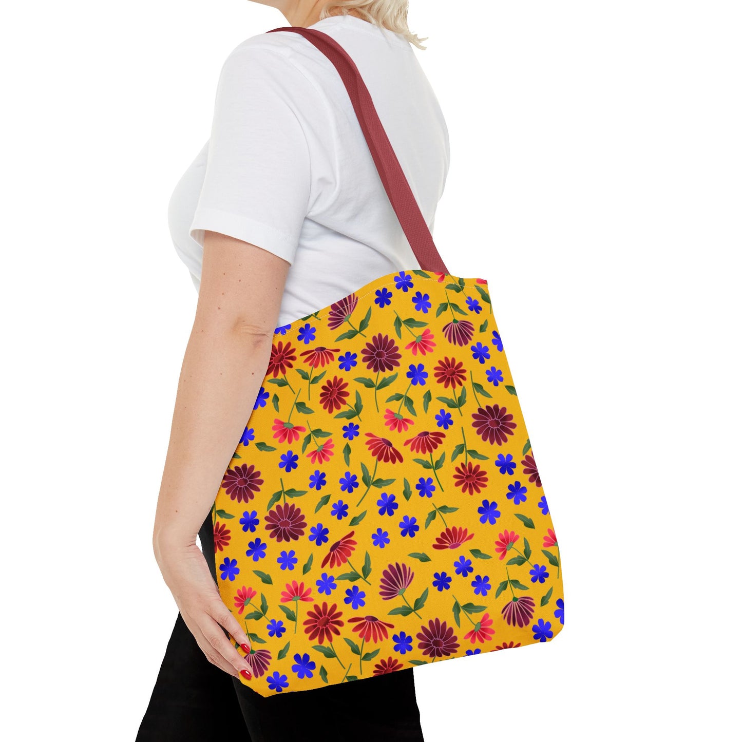 Person carrying the Golden Wildflower Tote Bag featuring a mustard-yellow backdrop with red, maroon daisies, and blue flowers, complemented by a solid red strap, embodying FireBrook Designs' joyful, practical style.