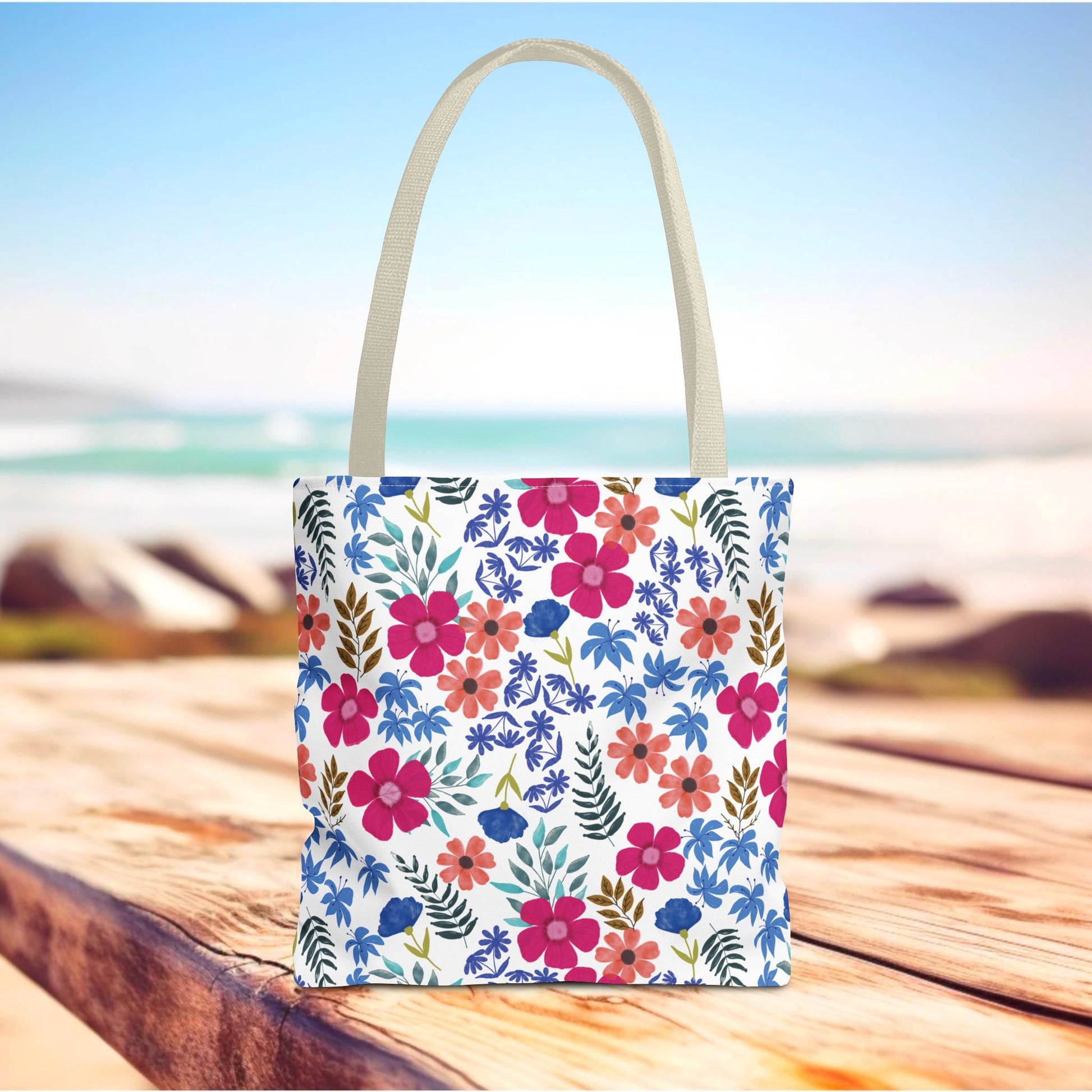Confetti Wildflower Tote Bag on a wooden deck with a colorful floral pattern, featuring bright flowers and green leaves, perfect for summer outings. Designed for durability with reinforced handles and boxed corners.