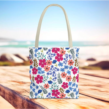 Confetti Wildflower Tote Bag on a wooden deck with a colorful floral pattern, featuring bright flowers and green leaves, perfect for summer outings. Designed for durability with reinforced handles and boxed corners.