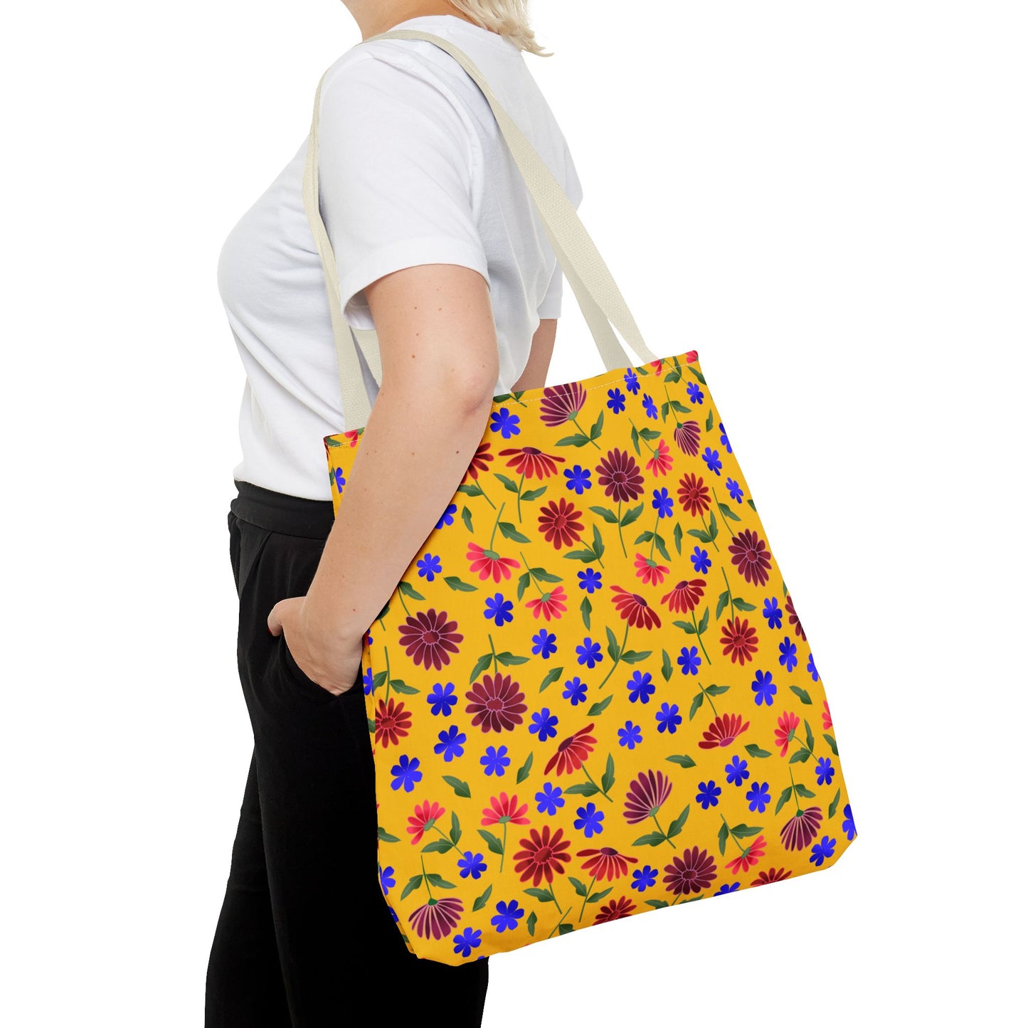 Person wearing a plain white T-shirt and black pants carries the Golden Wildflower Tote Bag, showcasing its bright yellow fabric adorned with red daisies, blue flowers, and green leaves.