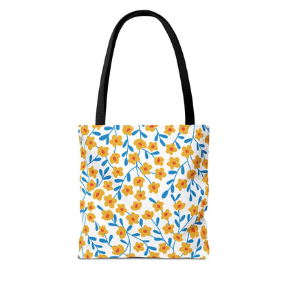 Buttercup Cream Tote Bag featuring a bright floral pattern of yellow flowers and blue leaves on a white backdrop, complemented by black straps, ideal for cheerful, stylish outings.