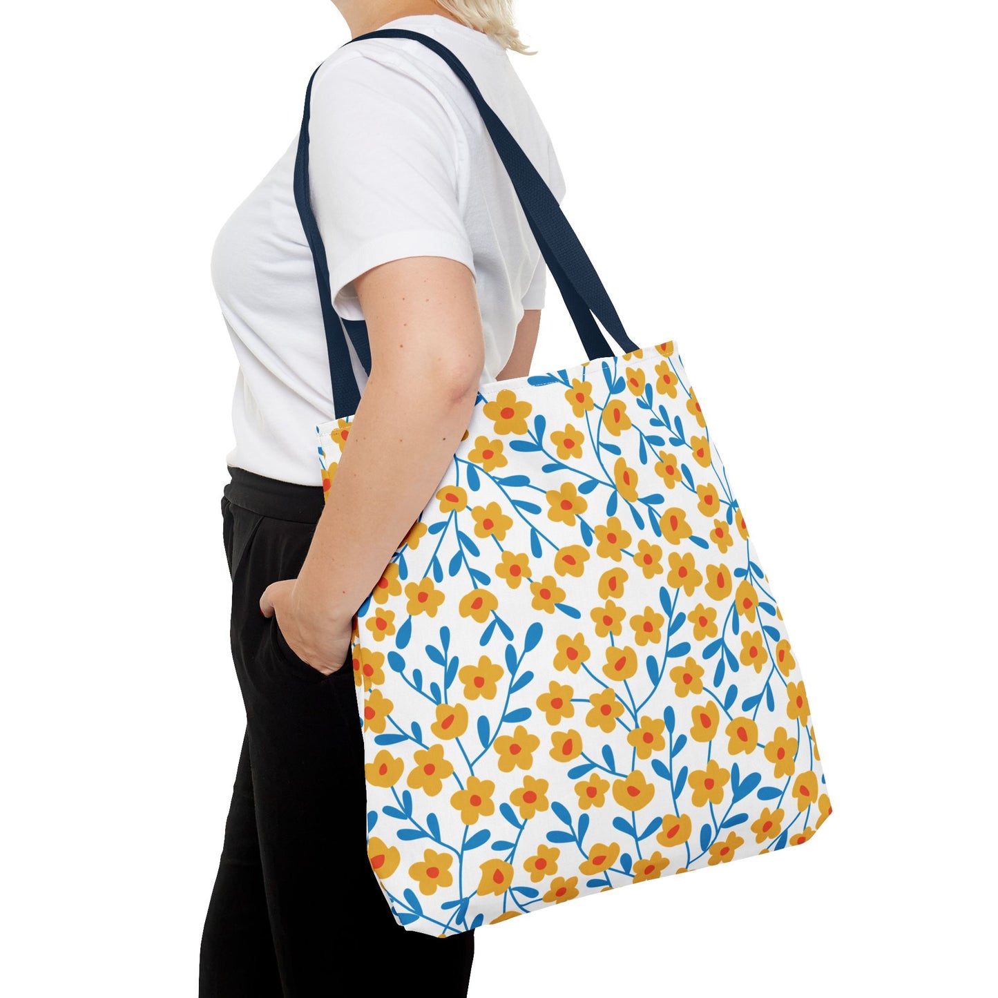 Floral Tote Bag featuring a vibrant pattern of stylized yellow flowers and blue leafy stems, carried by a person. This cheerful, versatile tote from FireBrook Designs is perfect for summer outings.