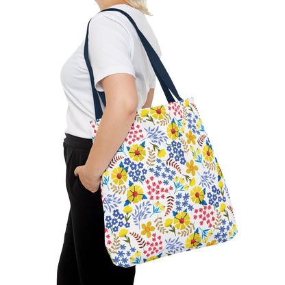 A person carries the Floral Tote Bag, showcasing its vibrant yellow, blue, and red floral pattern. Ideal for summer, this durable, stylish accessory embodies FireBrook Designs' uplifting and joyful aesthetic.