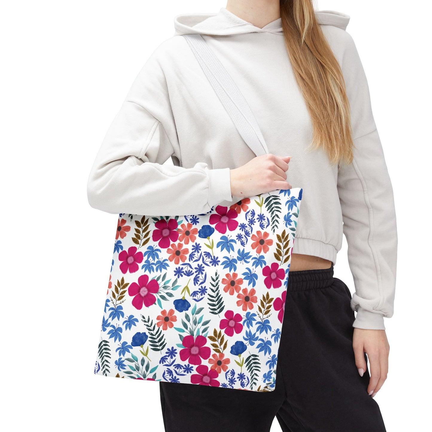 Floral Tote Bag featuring a vibrant floral print with pink, red, and blue blossoms, carried over the shoulder by a person in a light hoodie, perfect for brightening summer outings.