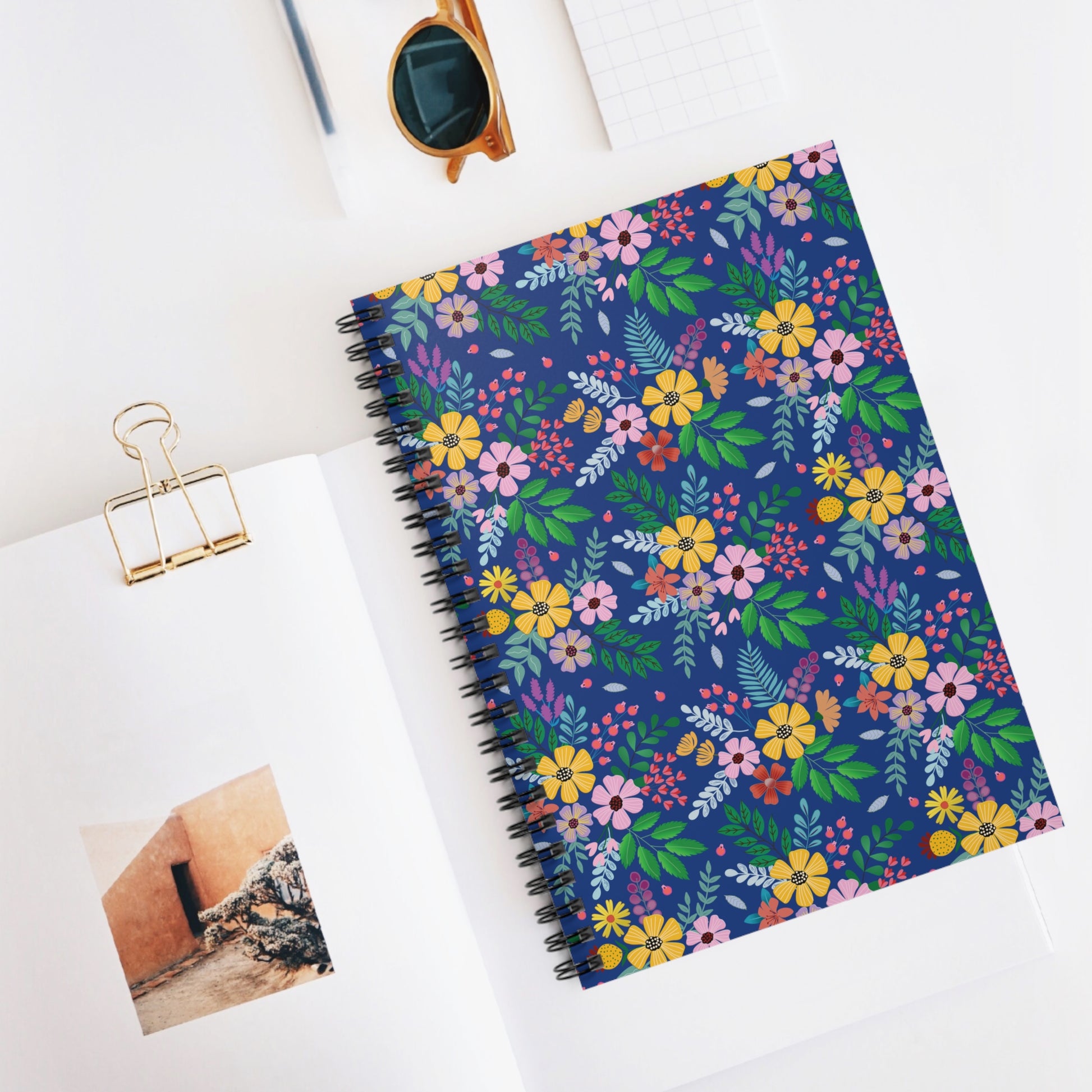 SPIRAL NOTEBOOK, DURABLE COVER, RULED, 6X8 – BOTANICAL BURST, featuring a multicolored floral pattern with a sturdy metal spiral, is perfect for on-the-go note-taking. Surrounded by stylish stationery items.